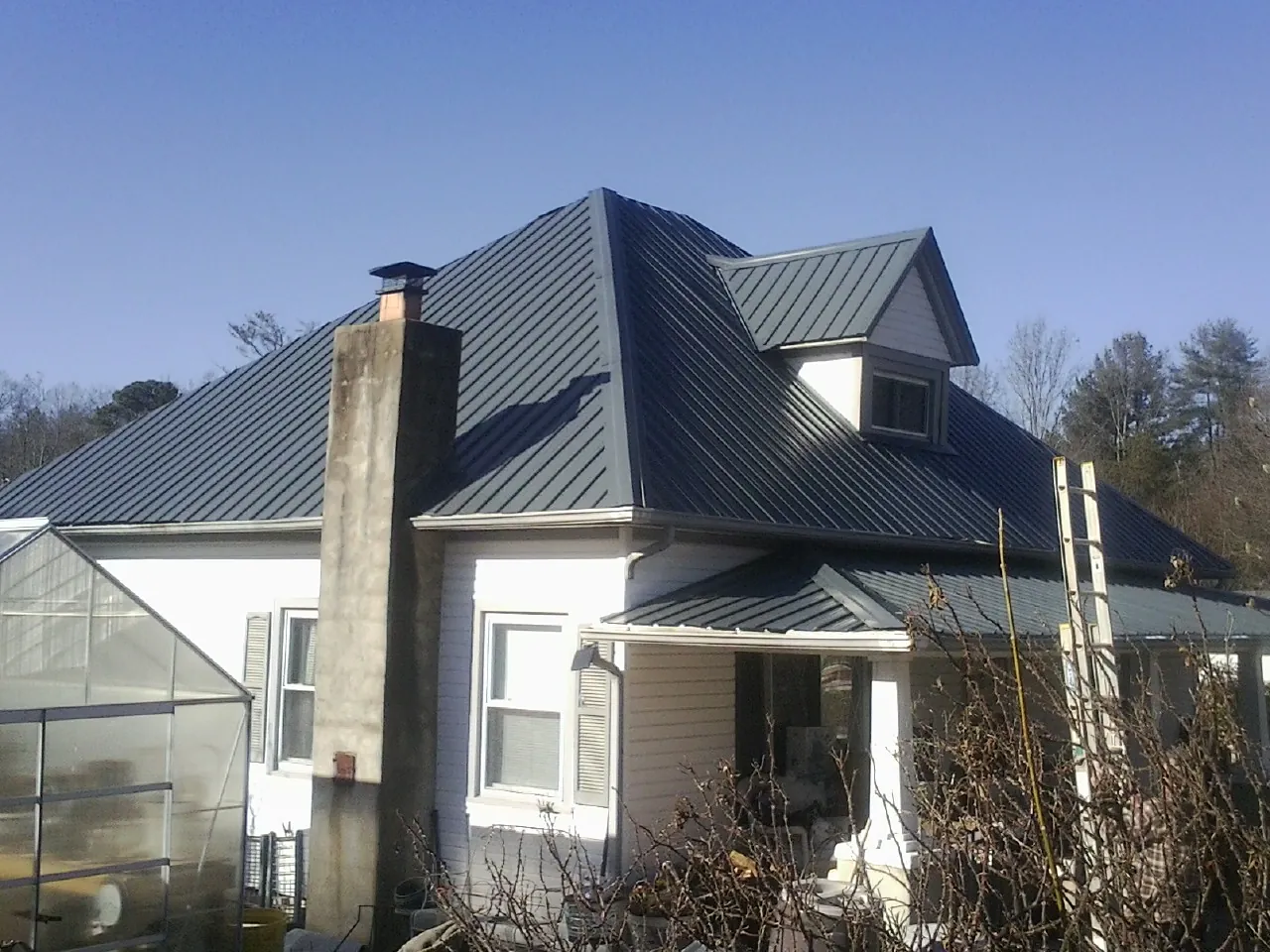 Dark blue standing seam metal roof on a white farmhouse with dormer — Slate & Tile Roof Repair by Roofing Brothers in North Fairfield