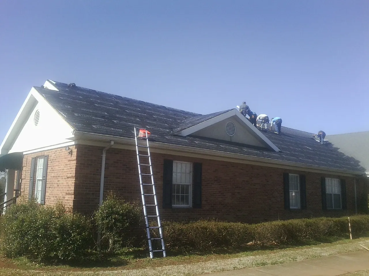 Crew tearing shingles off a brick ranch roof with a ladder set — Emergency Roof Repair work by our crew in North Fairfield