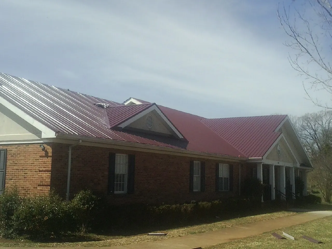 Red metal roof with gabled entries on a long brick building, from a Hail Damage Roof Repair job in North Fairfield