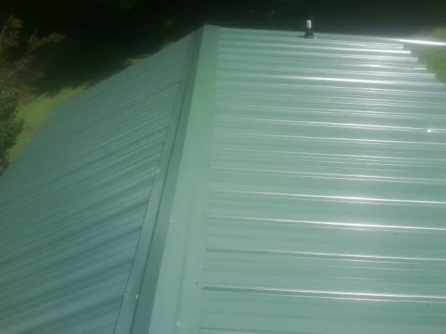 New green metal panels meeting at the ridge of a roof — Flat Roof Repair work by our crew in North Fairfield
