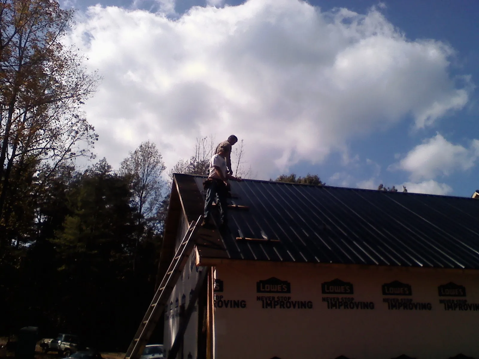 Roofer fastening dark metal panels high against a cloudy sky, from a Roof Inspection job in North Fairfield