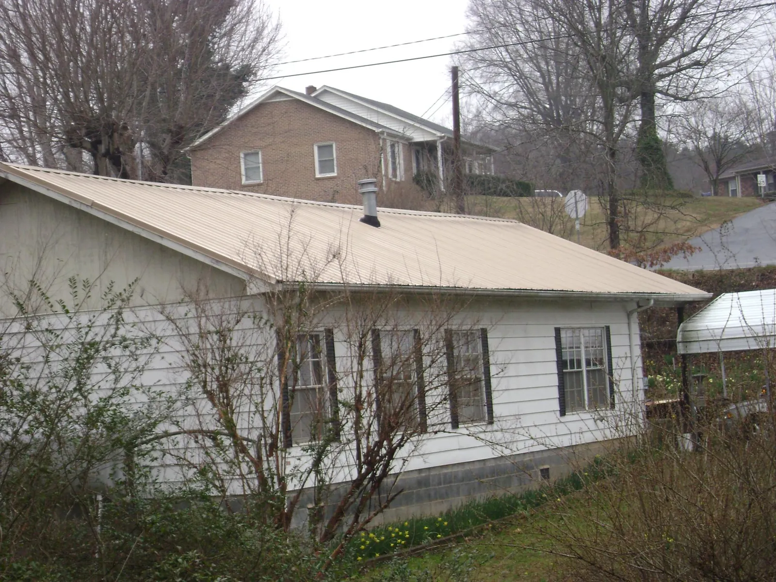 Tan metal roof on a white sided house set into a hillside — Commercial Roofing by Roofing Brothers in North Fairfield