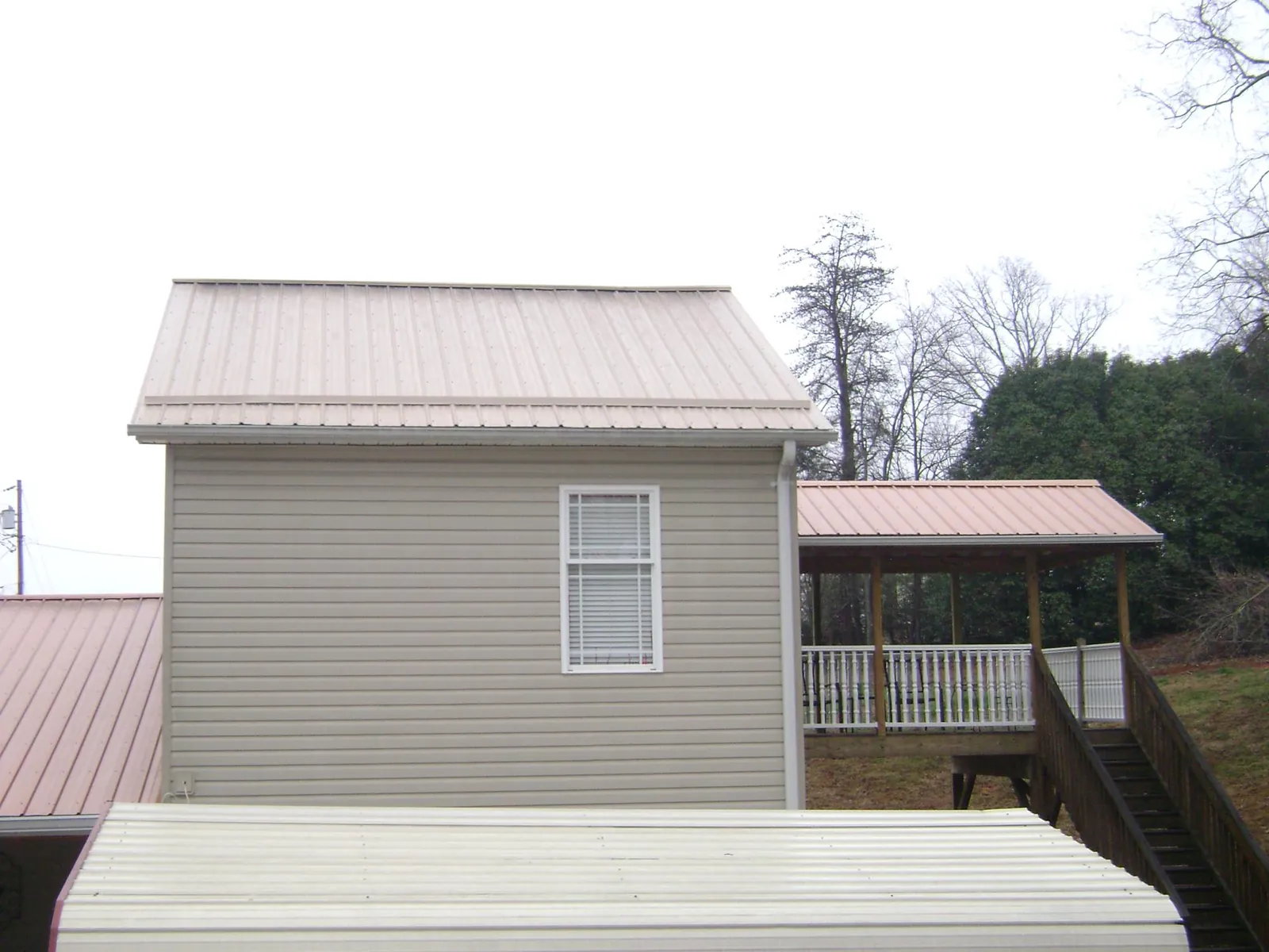 Tan metal roofs on a two story addition and attached porch, from a Roof Replacement job in North Fairfield